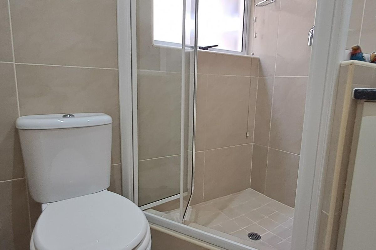 A functional bathroom featuring a tiled shower enclosure with a glass door, a standard toilet, and a vanity unit.