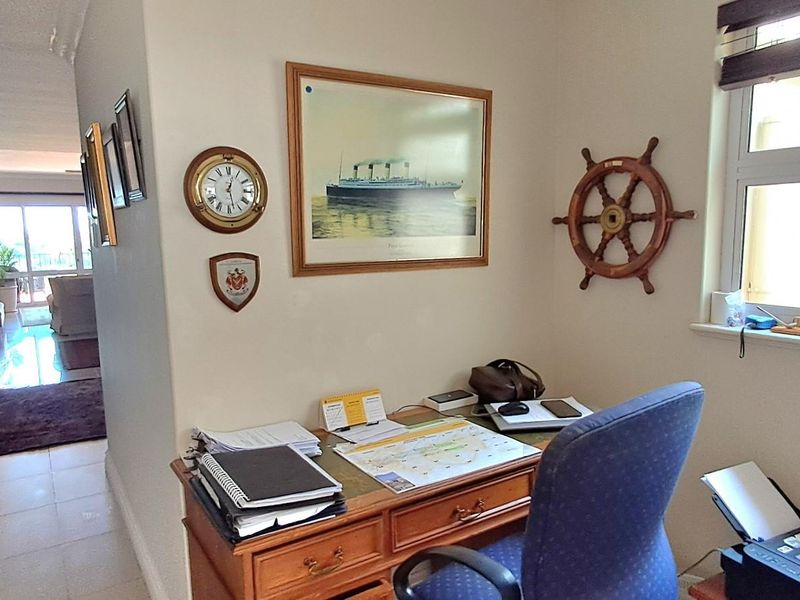 A functional home office space featuring tiled flooring and a window, with an open-plan layout leading into the main living area.