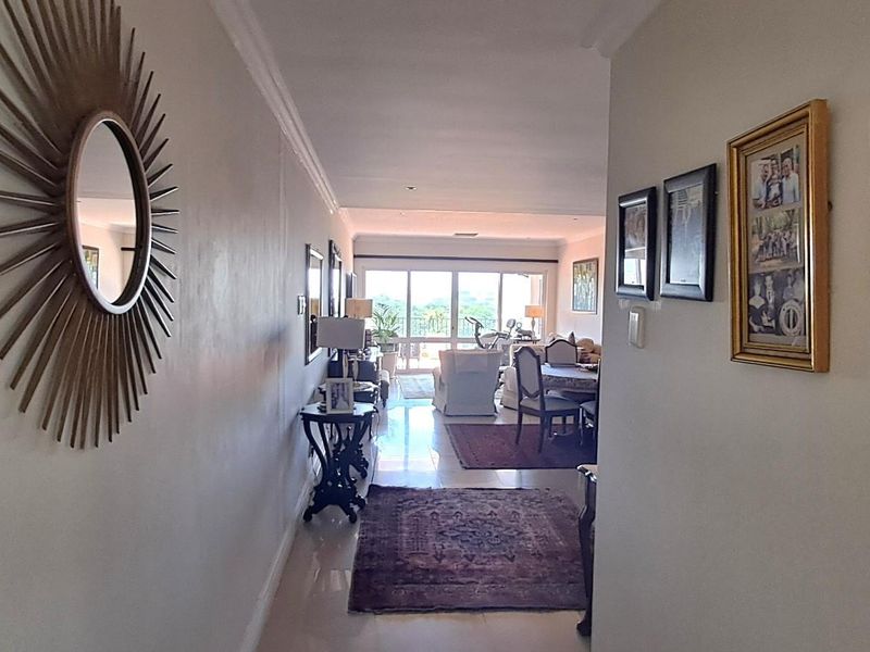 A view from the hallway looking through to the open plan living and dining area, featuring tiled flooring and access to a balcony.