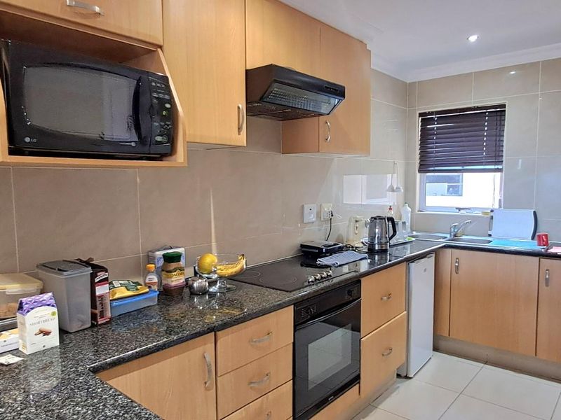 Functional kitchen featuring light wood cabinetry, granite countertops, built-in oven, electric hob, extractor fan, and tiled splashbacks.