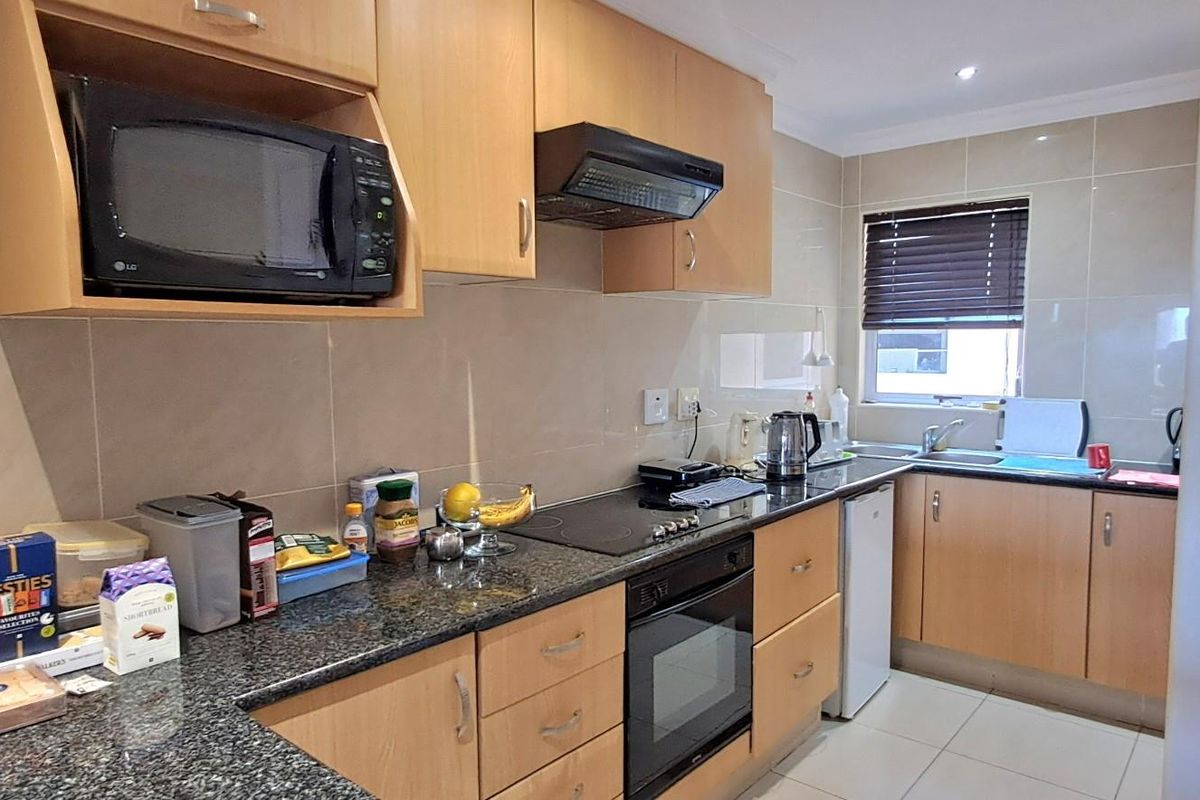 Functional kitchen featuring light wood cabinetry, granite countertops, built-in oven, electric hob, extractor fan, and tiled splashbacks.