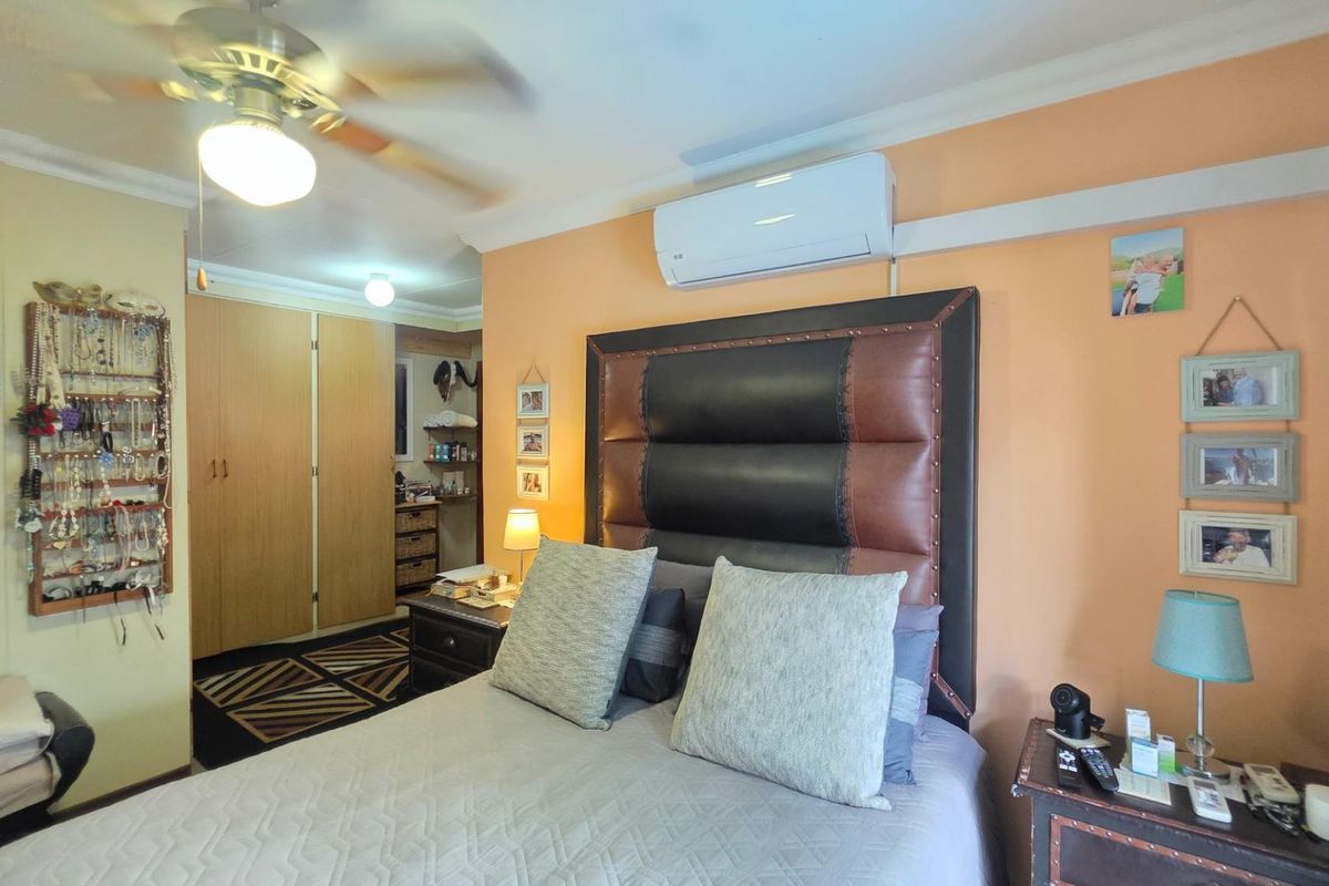 A bedroom featuring built-in cupboards, a ceiling fan, and a wall-mounted split-system air conditioning unit.