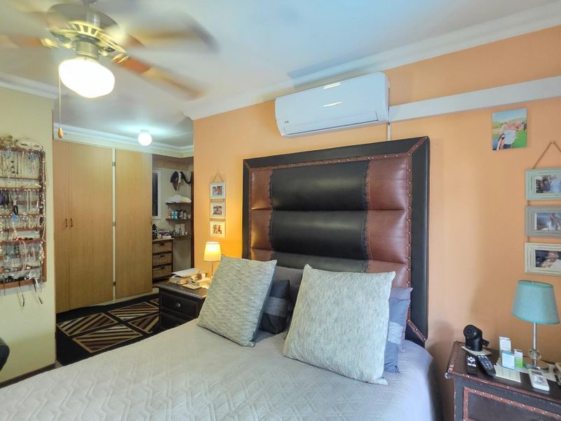 A bedroom featuring built-in cupboards, a ceiling fan, and a wall-mounted split-system air conditioning unit.
