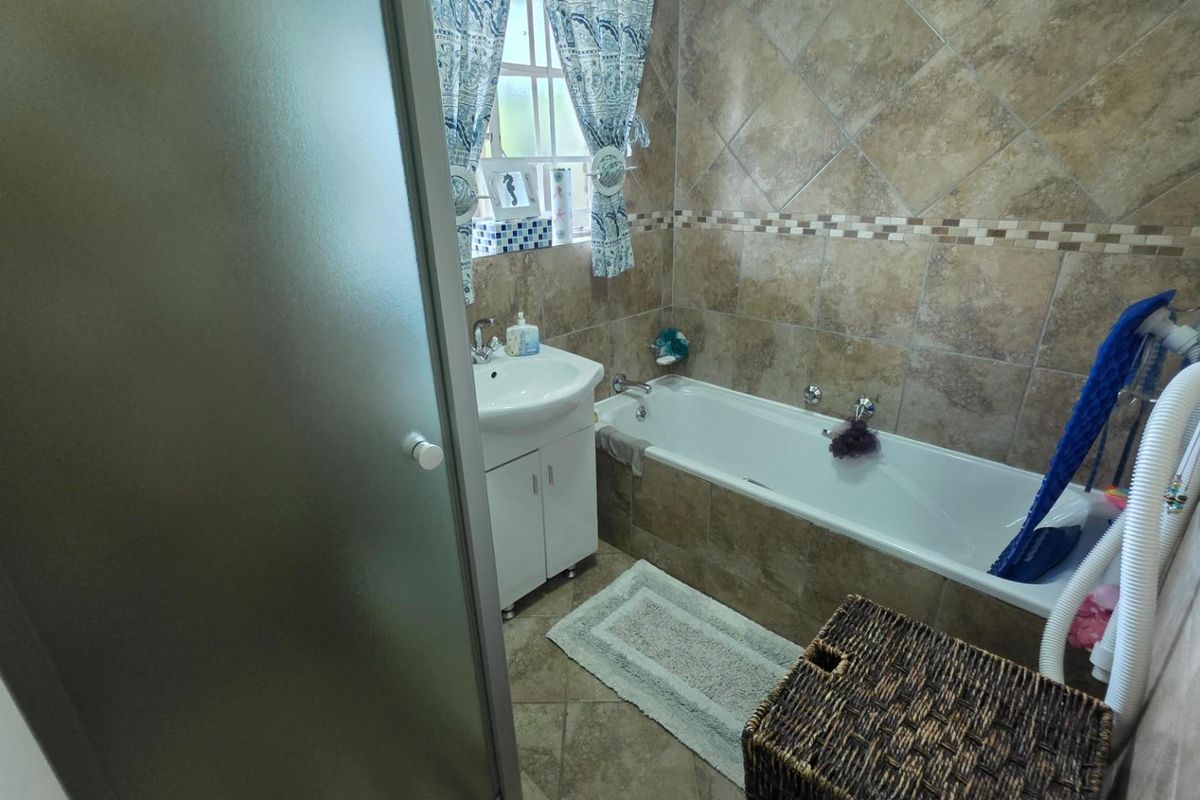 A functional bathroom featuring a bathtub, vanity basin, and neutral-toned wall and floor tiling.