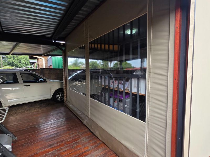 A covered patio area featuring timber decking, a corrugated metal roof, and protective outdoor blinds, providing a versatile space for outdoor living.