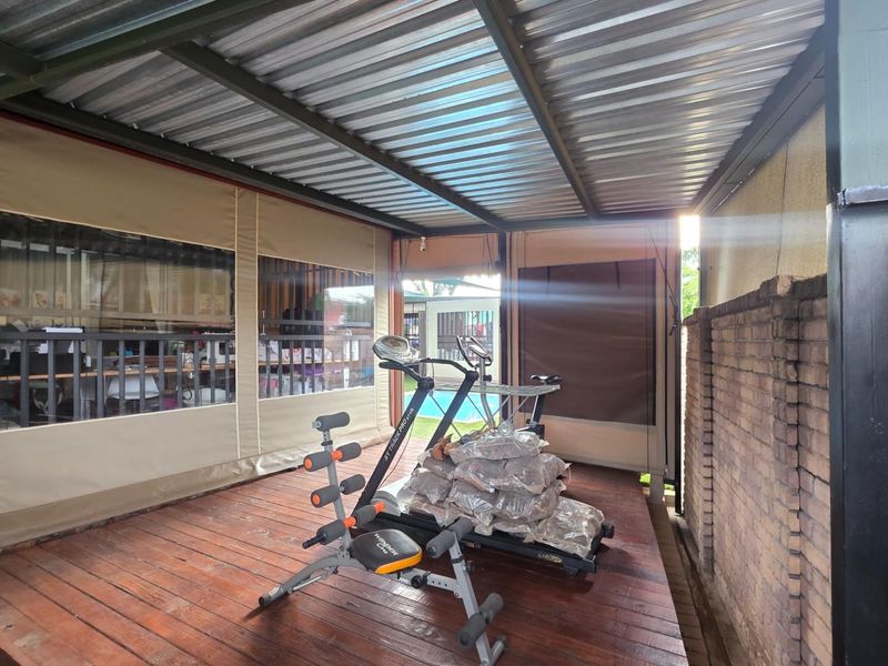 A covered outdoor patio area featuring timber decking, a corrugated metal roof, and protective canvas roll-up blinds, providing a versatile space for outdoor living.