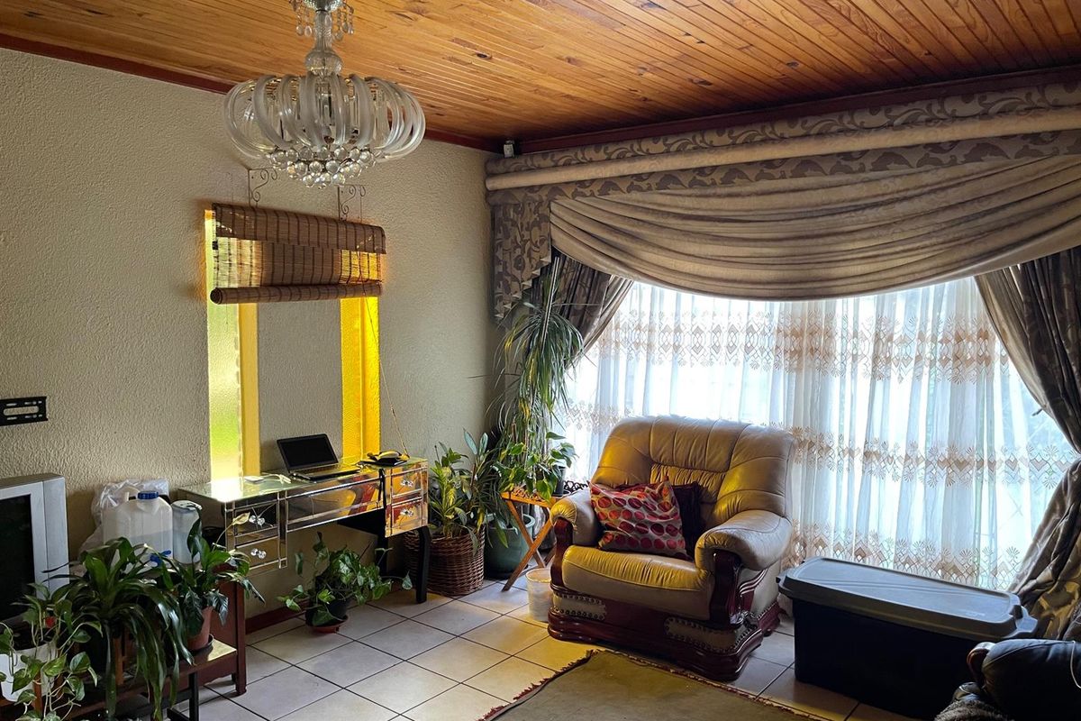 A living room featuring a timber-paneled ceiling, tiled flooring, and large windows with heavy drapery.
