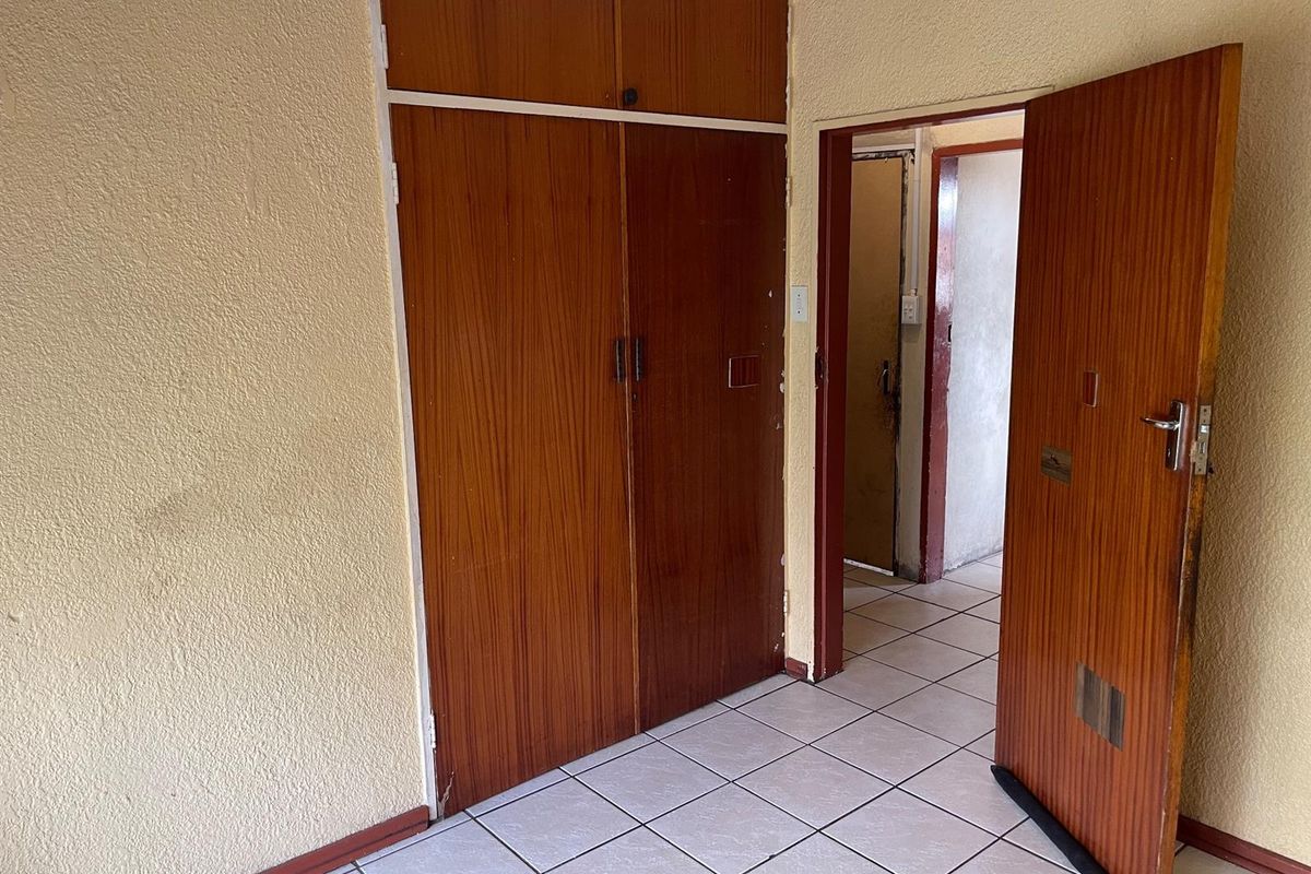An empty bedroom featuring built-in wooden cupboards, tiled flooring, and access to an adjoining hallway.