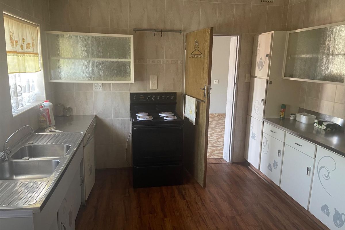 A functional kitchen featuring built-in cabinetry, a double stainless steel sink, and a freestanding electric stove with tiled splashbacks.