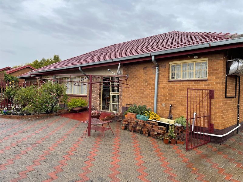 Rear view of a brick house featuring a paved courtyard, security gate, and tiled roof.