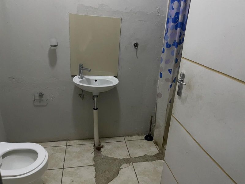 A functional bathroom featuring a wall-mounted basin, toilet, and shower area, currently requiring cosmetic repairs to the flooring and wall finishes.
