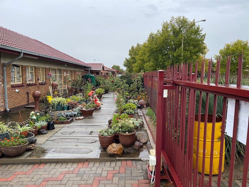 A view of the side exterior walkway featuring brick paving, a red metal security fence, and access to the side of the house.