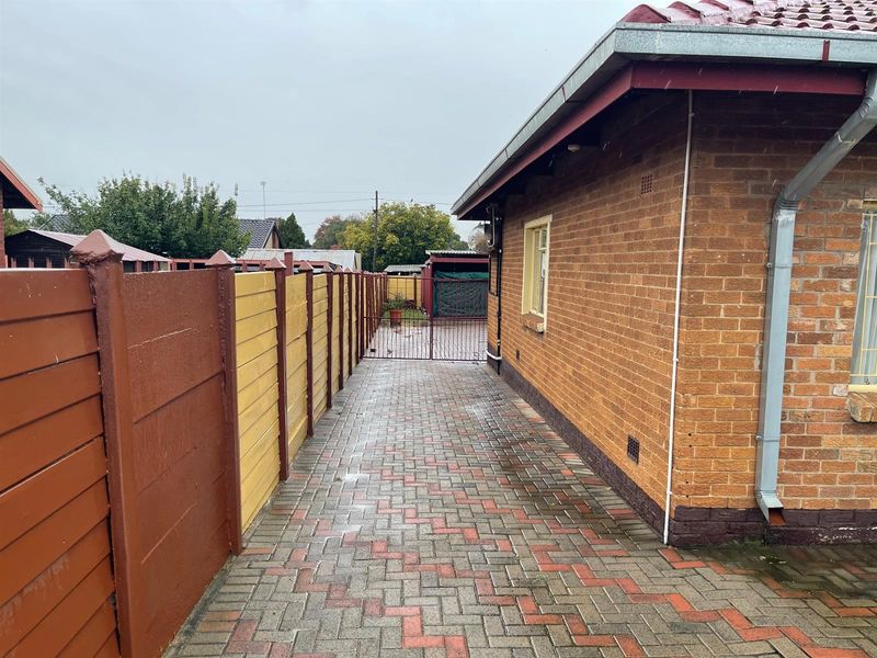 A side exterior view of the property featuring paved walkway, brick facade, and painted boundary fencing leading to a rear gate.