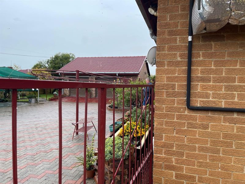 View of the rear yard featuring a paved driveway, brick exterior wall, and a detached garage structure.