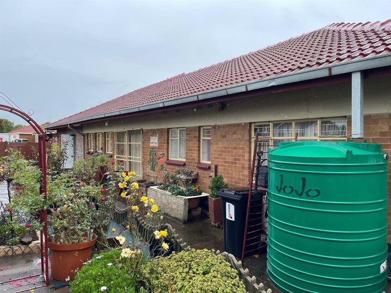 Rear exterior view of the house featuring brick facade, tiled roof, security bars on windows, and a large water storage tank.