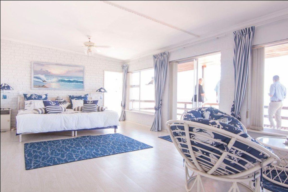 Spacious bedroom featuring white painted brick walls, large windows, and sliding glass doors leading to an outdoor balcony area.