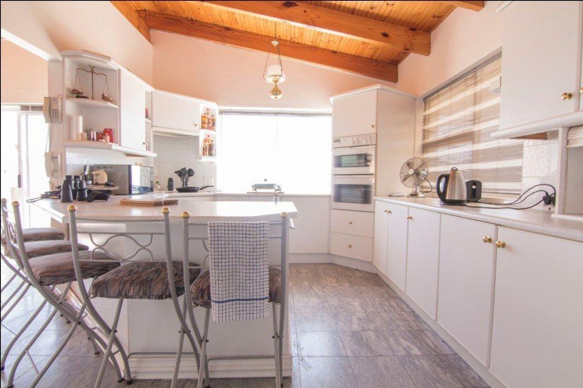A functional kitchen featuring white cabinetry, built-in oven, microwave, and a breakfast bar, complemented by a vaulted timber-beamed ceiling.