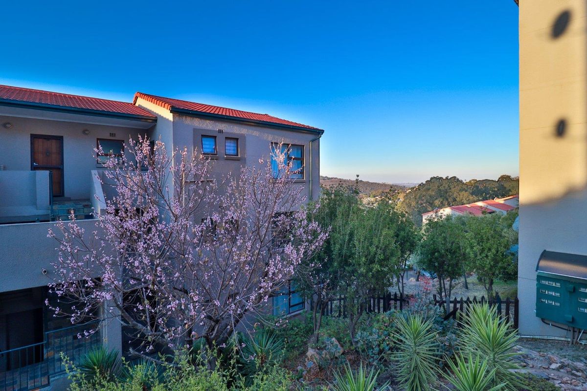 Rear view of the apartment building featuring a balcony, terracotta roof tiles, and landscaped garden area with scenic views.
