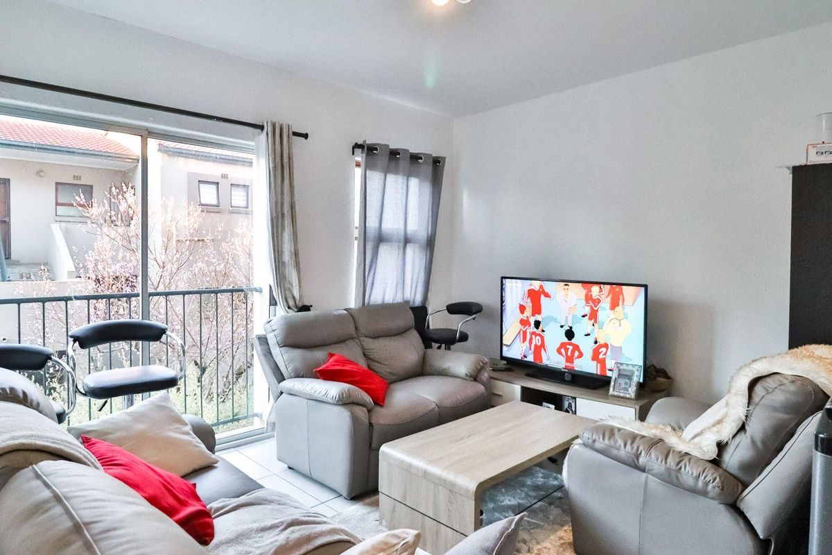 A functional living room featuring tiled flooring and a sliding glass door that opens onto a balcony, providing natural light to the space.