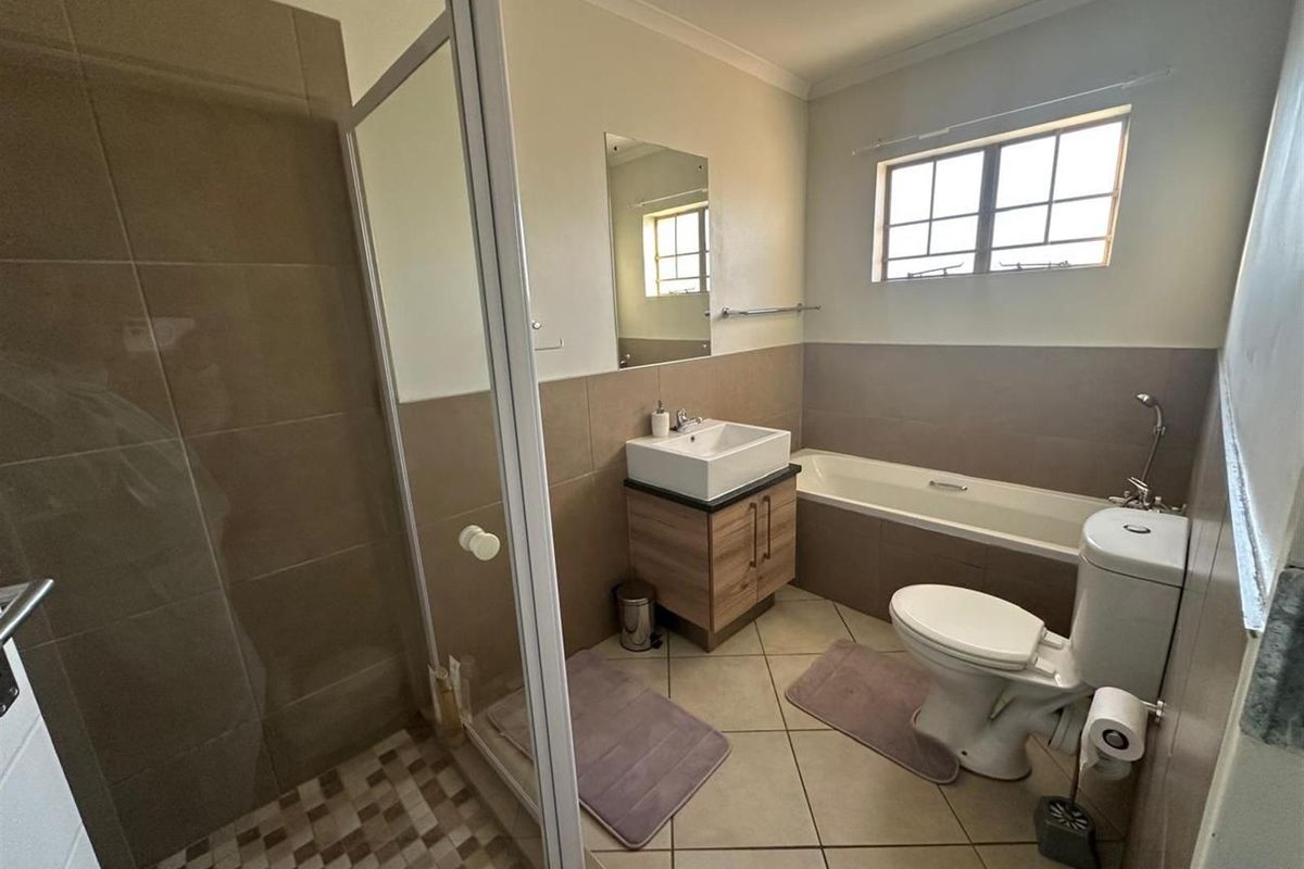 A well-maintained bathroom featuring a separate glass-enclosed shower, a bathtub, a vanity basin, and a toilet with neutral tiled finishes.