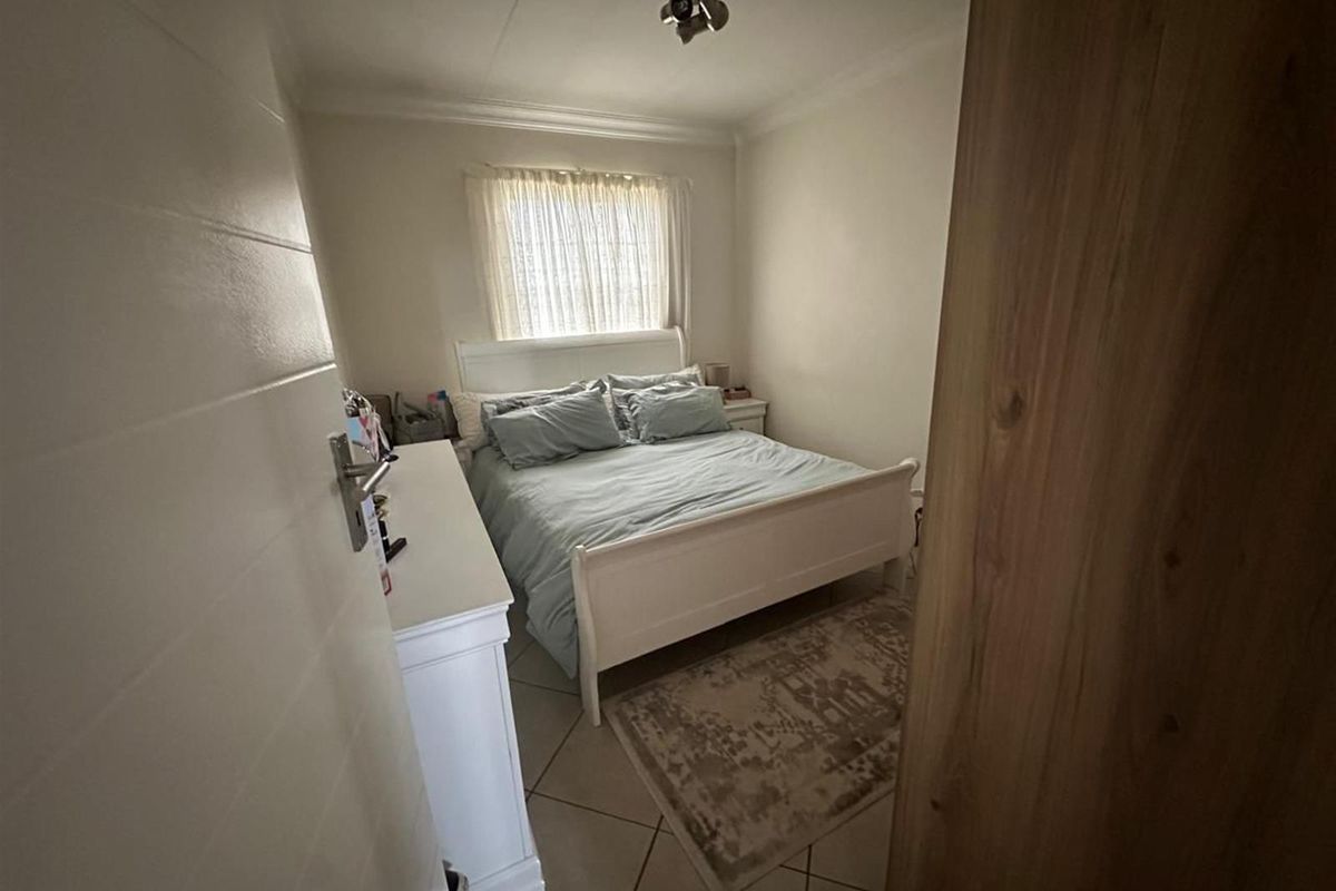 A compact bedroom featuring tiled flooring, a window with sheer curtains, and a central ceiling light fixture.