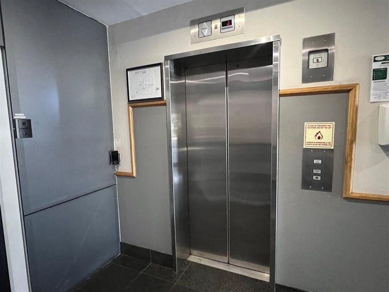 A functional office building elevator lobby featuring stainless steel elevator doors, tiled flooring, and integrated access control systems.