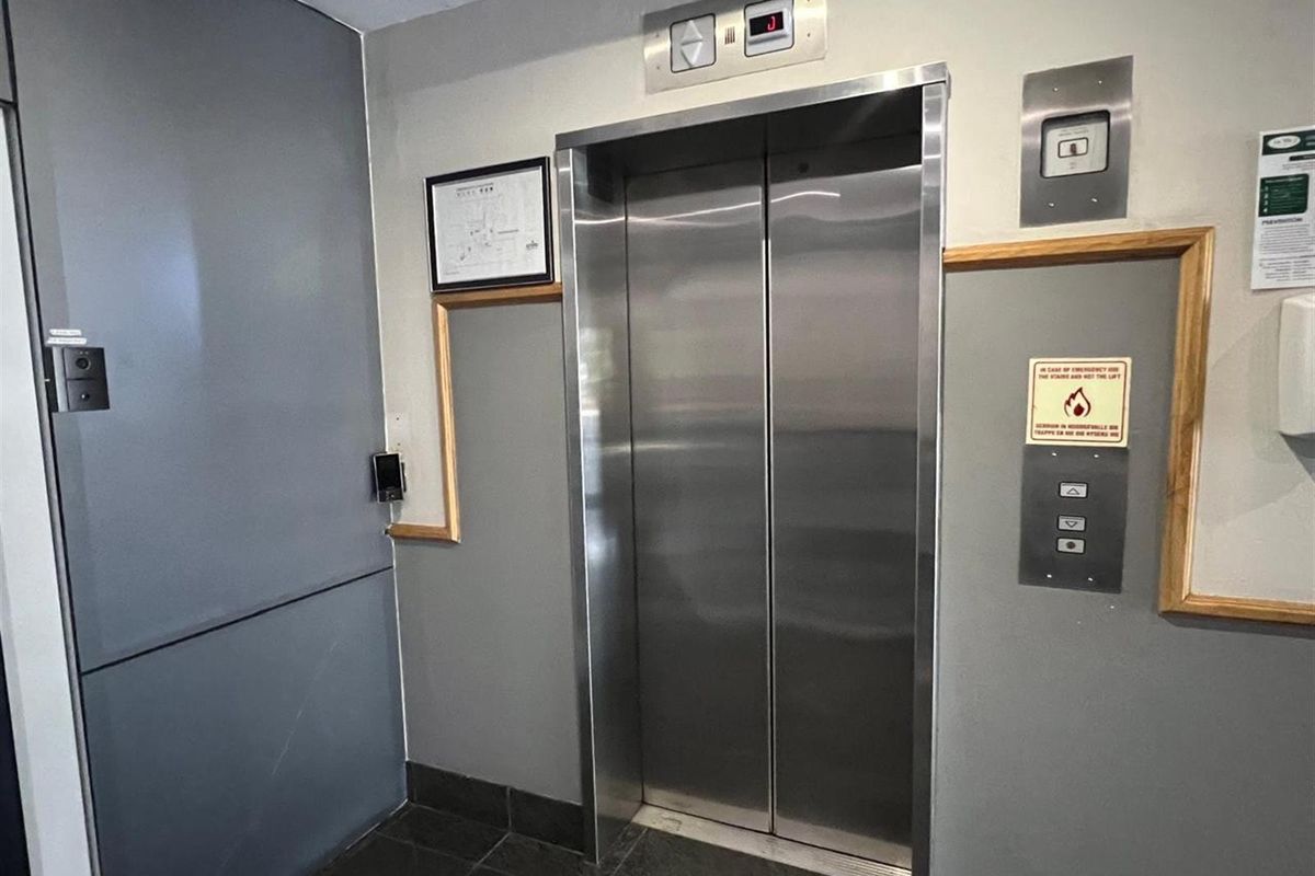 A functional office building elevator lobby featuring stainless steel elevator doors, tiled flooring, and integrated access control systems.