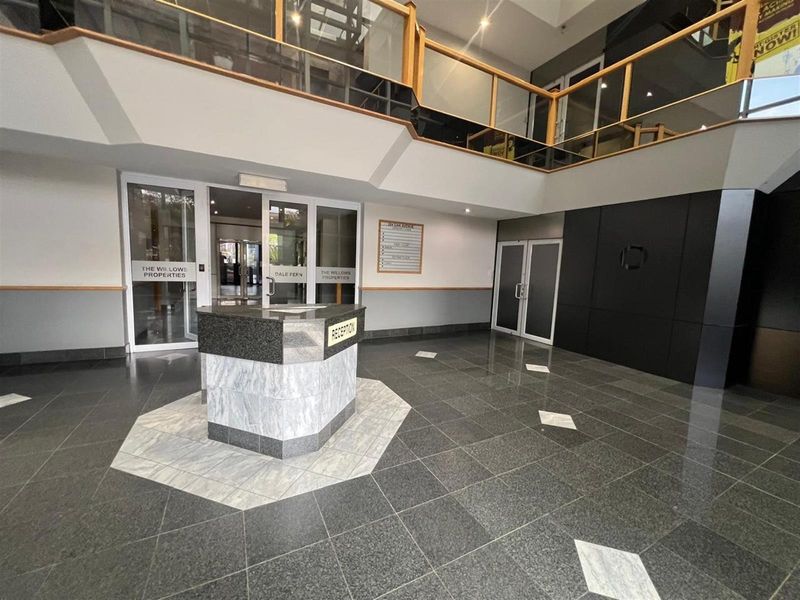 Spacious office building reception area featuring a central stone reception desk, polished tile flooring, and a mezzanine level with wooden railings.