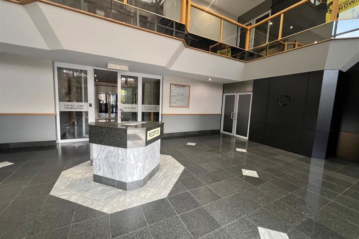 Spacious office building reception area featuring a central stone reception desk, polished tile flooring, and a mezzanine level with wooden railings.