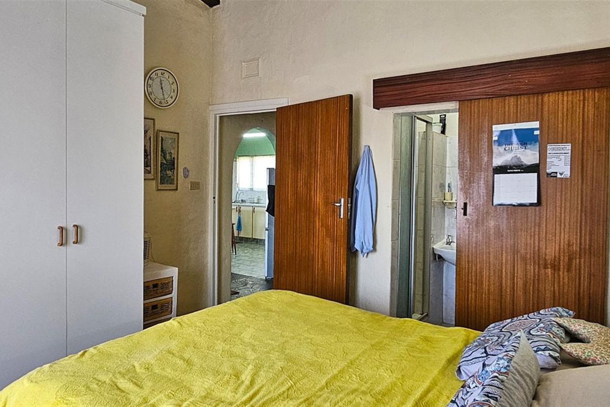 A bedroom featuring built-in wardrobes and an en-suite bathroom, with a doorway leading through to the kitchen area.