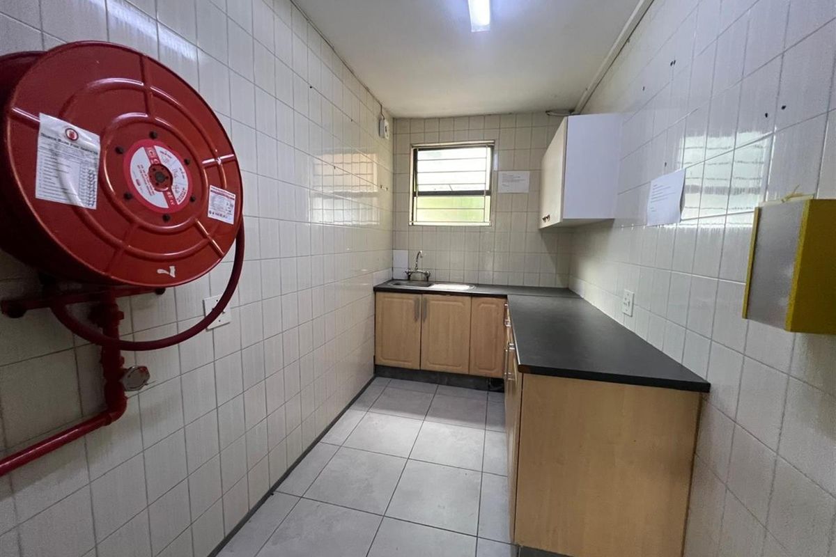 A functional office kitchenette featuring tiled walls, built-in cabinetry with laminate countertops, a stainless steel sink, and a wall-mounted fire hose reel.