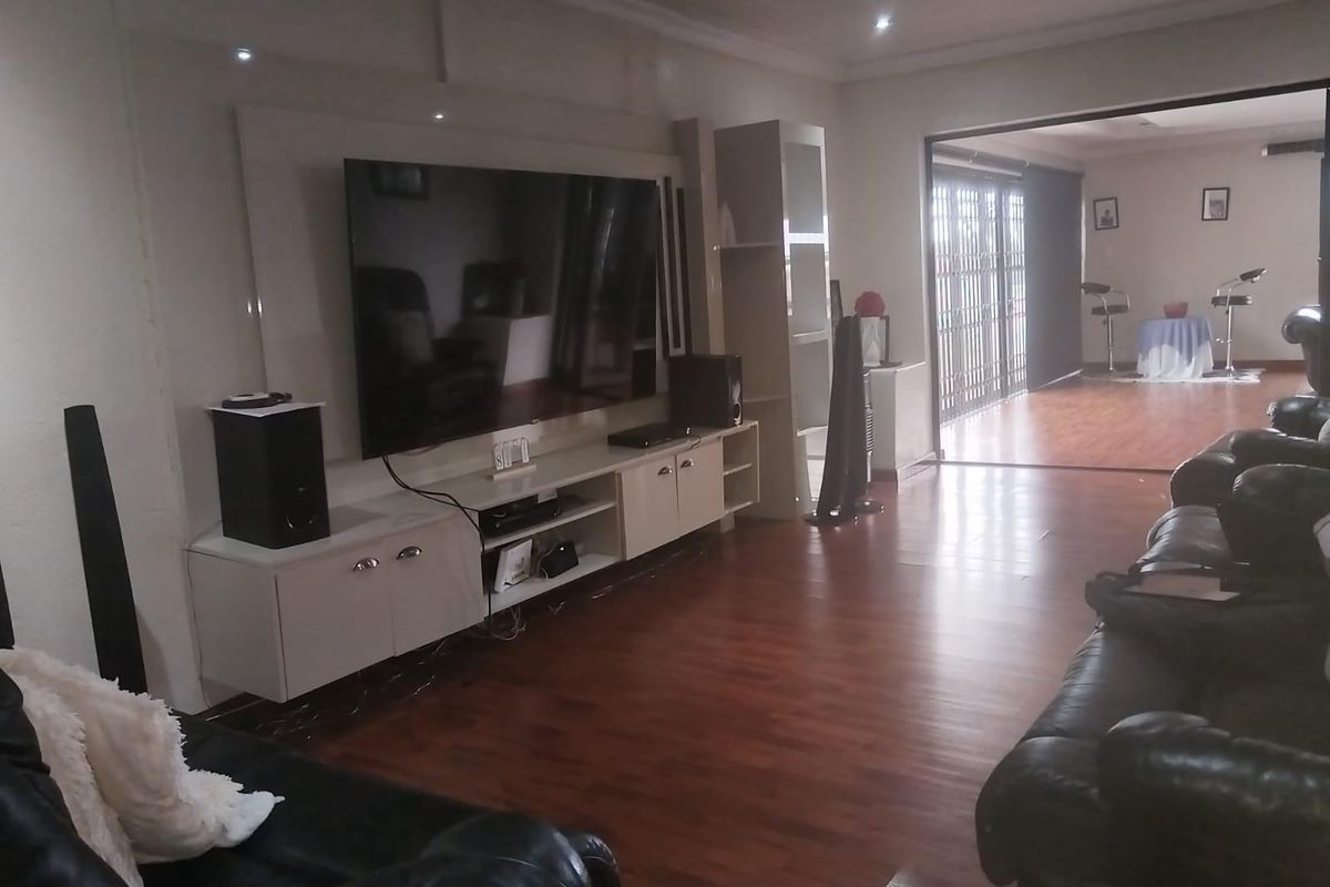 Spacious living area featuring wood-look flooring, recessed ceiling lighting, and a built-in media console unit, leading into an adjacent sunroom or patio area.