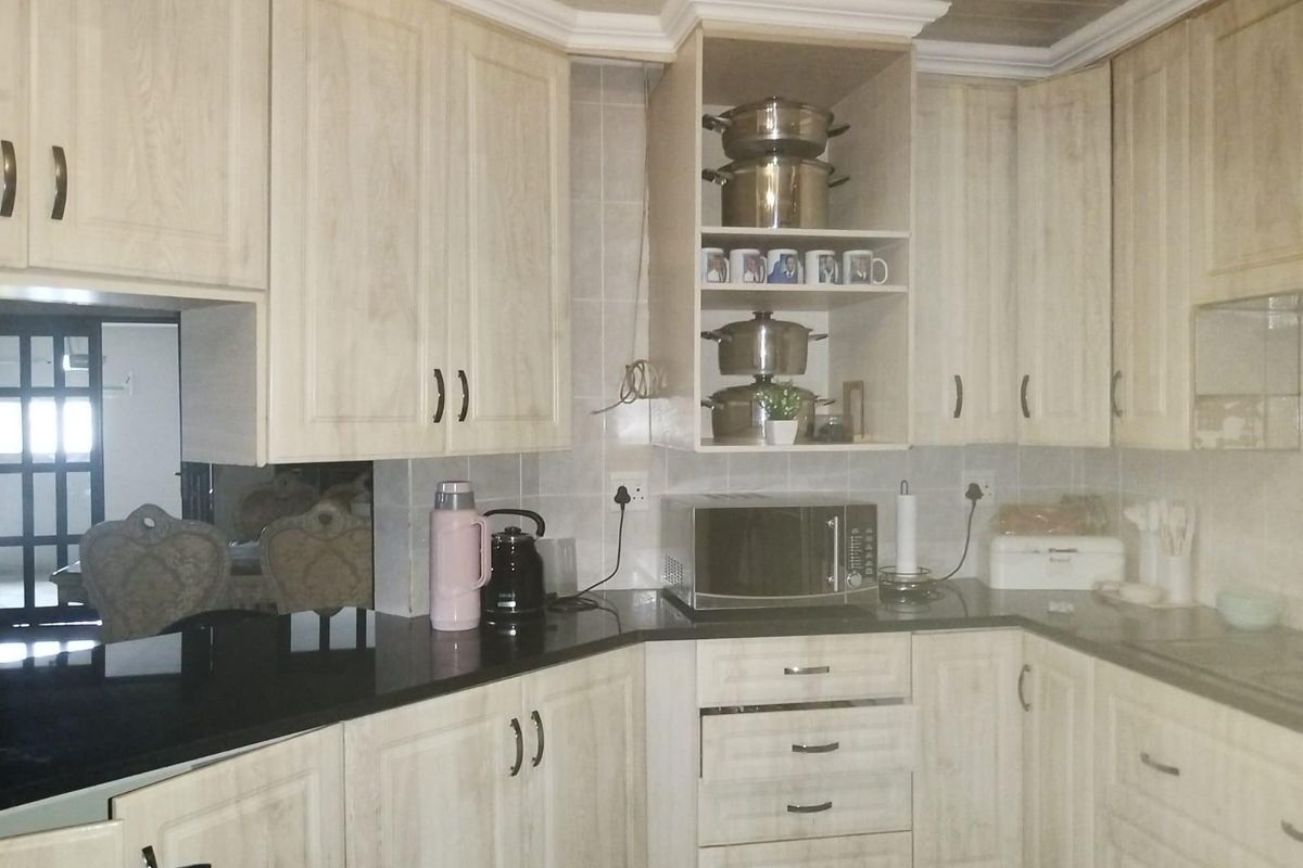 A functional kitchen featuring light wood-grain cabinetry, dark granite countertops, and a tiled backsplash, offering ample storage and workspace.