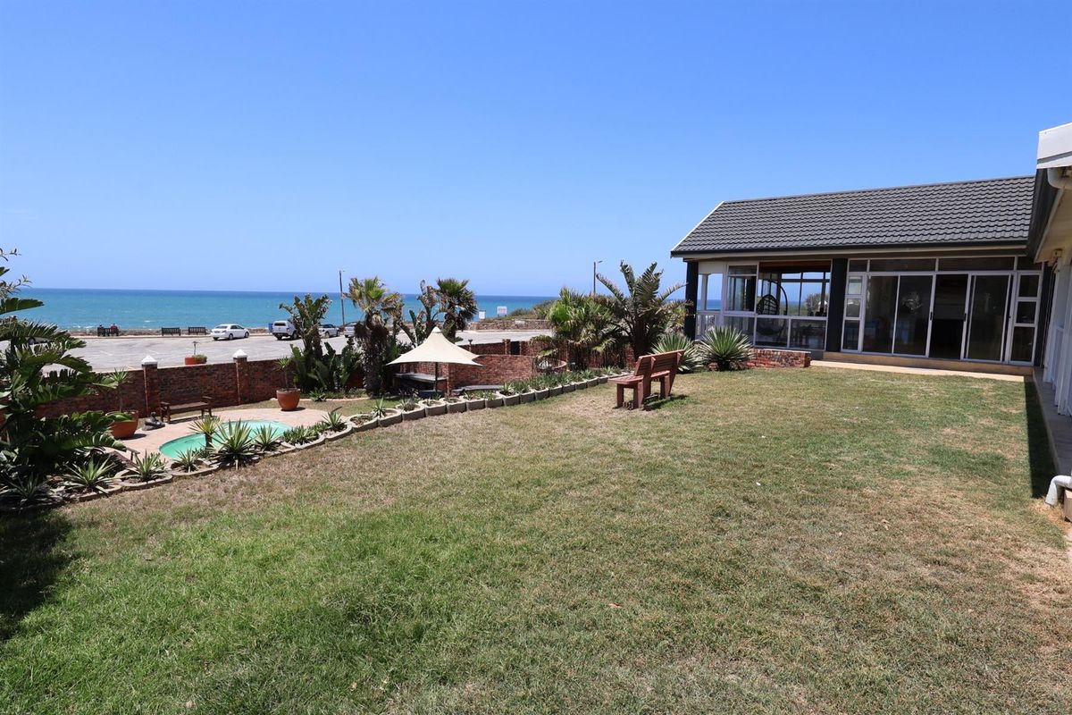 A spacious rear garden featuring a swimming pool, brick boundary wall, and direct views of the ocean and coastal road.