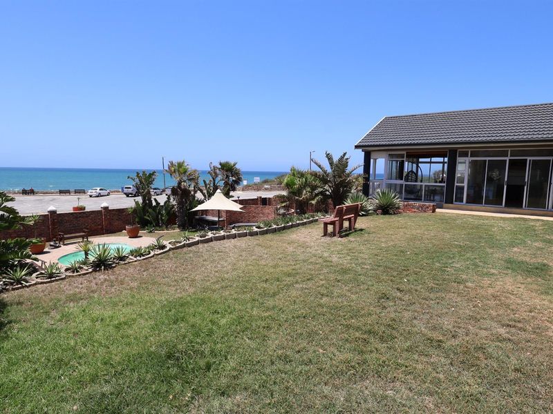 A spacious rear garden featuring a swimming pool, brick boundary wall, and direct views of the ocean and coastal road.