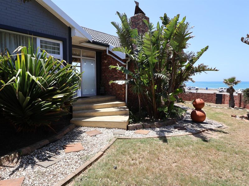 Front entrance area featuring a brick chimney, concrete steps, and landscaped garden with ocean views in the background.