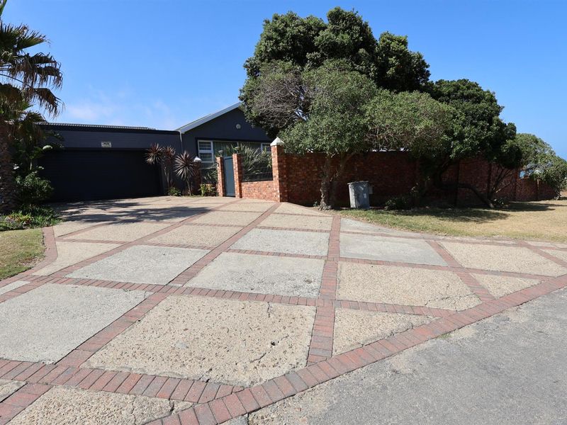 Front exterior view featuring a paved driveway, brick boundary wall, and a double garage, set within a landscaped garden area.