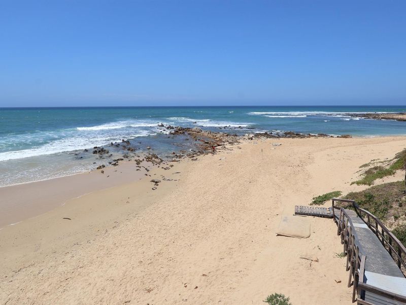 A scenic coastal view overlooking a sandy beach with rocky outcrops and a wooden boardwalk leading towards the shoreline.