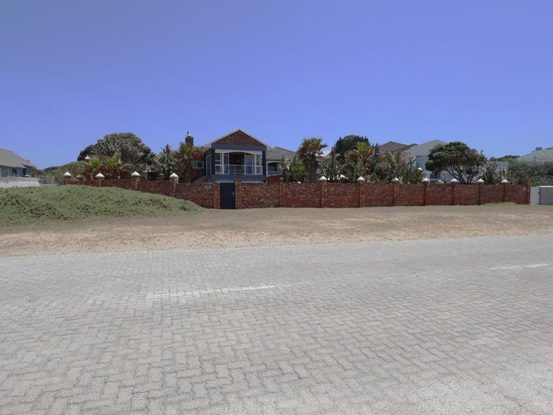 A street-level view of the property featuring a prominent brick boundary wall, landscaped garden, and a raised dwelling with a covered balcony.