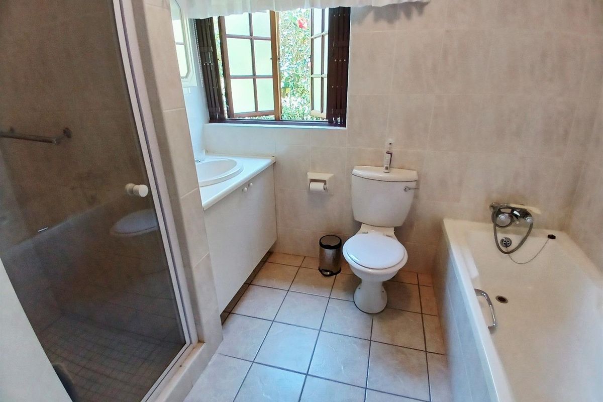 A functional bathroom featuring a separate shower cubicle, a built-in vanity with basin, a toilet, and a bathtub with a handheld shower attachment.
