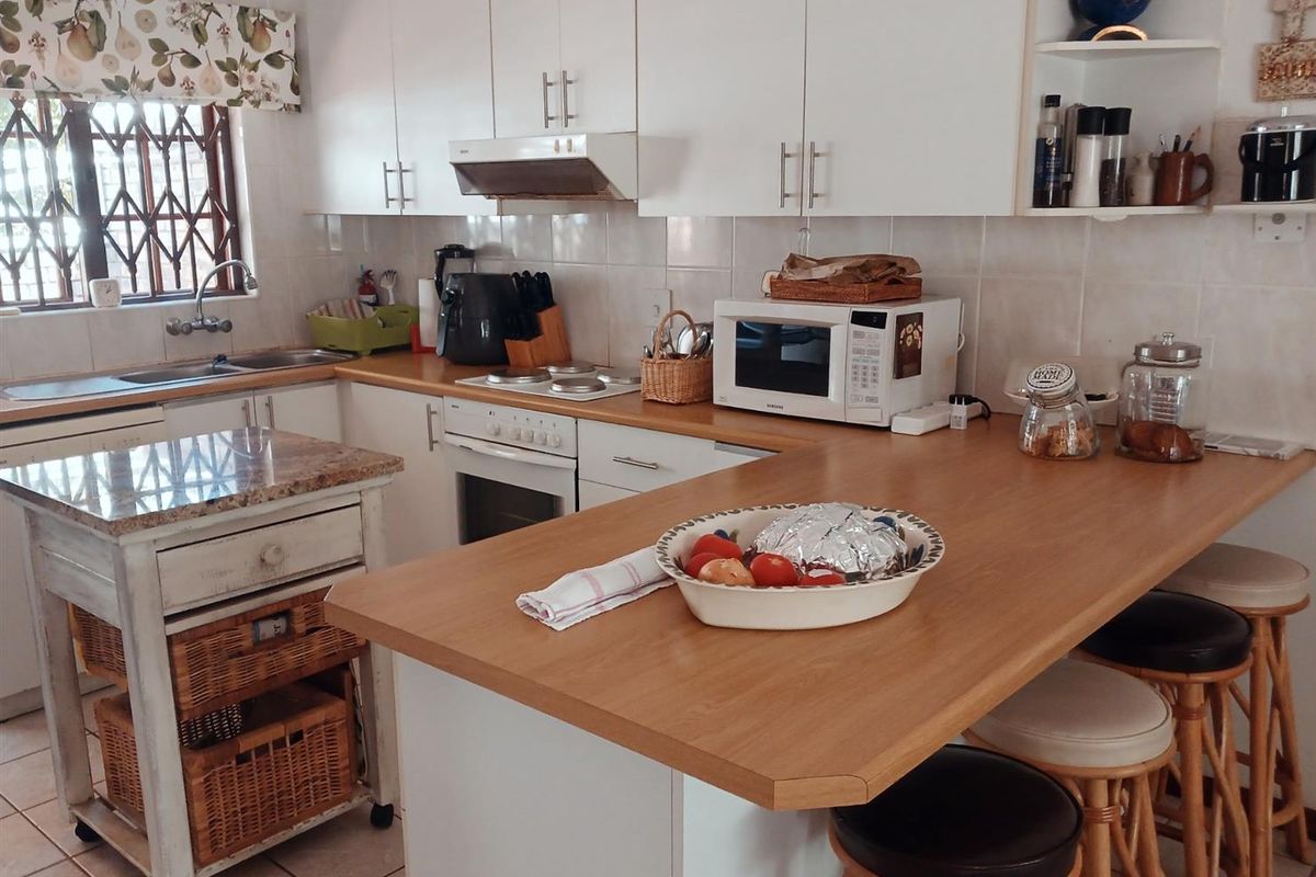 A functional kitchen featuring white cabinetry, a breakfast bar, tiled backsplash, and a stainless steel sink with a window view.