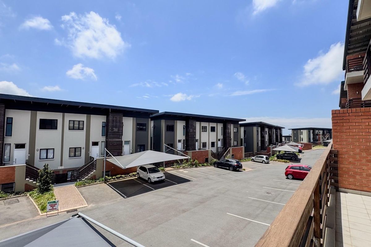 An elevated view of a modern apartment complex featuring paved parking areas, shade-cloth carports, and contemporary multi-story residential buildings with brick and plaster finishes.