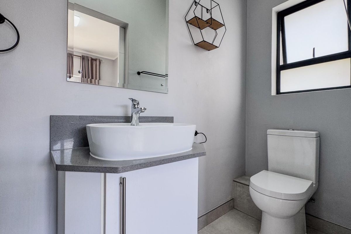A modern bathroom featuring a white vanity with a stone countertop, vessel sink, wall-mounted mirror, and a standard toilet.