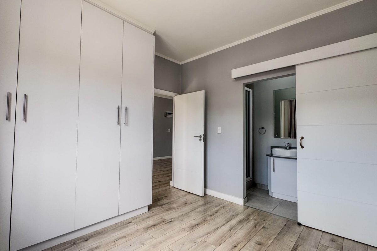 A bedroom featuring built-in wardrobes, wood-look flooring, and a sliding door providing access to an en-suite bathroom.