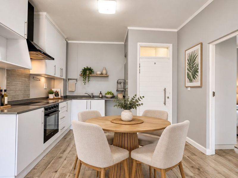 A modern open-plan kitchen and dining area featuring sleek white cabinetry, integrated appliances, and light wood-look laminate flooring, leading into a bedroom.