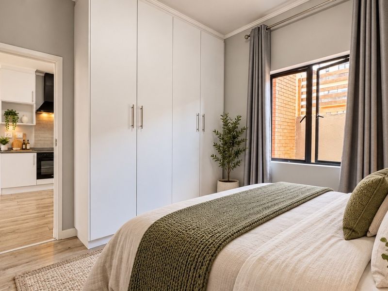 A well-maintained bedroom featuring built-in cupboards, laminate flooring, and a view through to the kitchen area.