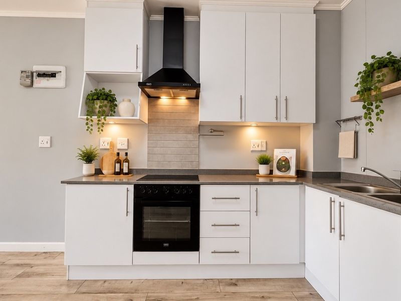 Modern kitchen featuring white cabinetry, stone countertops, integrated oven and hob, extractor fan, and a stainless steel sink with tiled splashback.