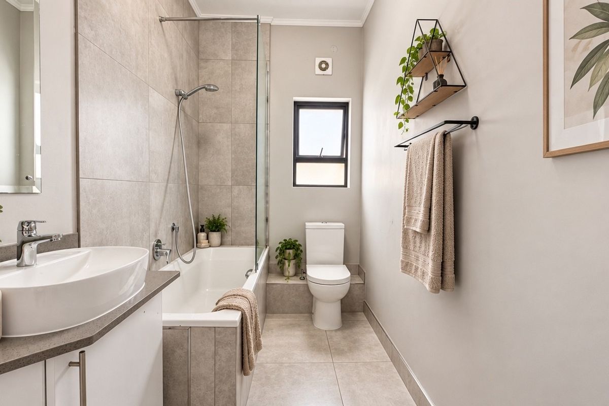 Modern bathroom featuring a built-in vanity, basin, bathtub with shower screen, and toilet, finished with neutral floor and wall tiling.