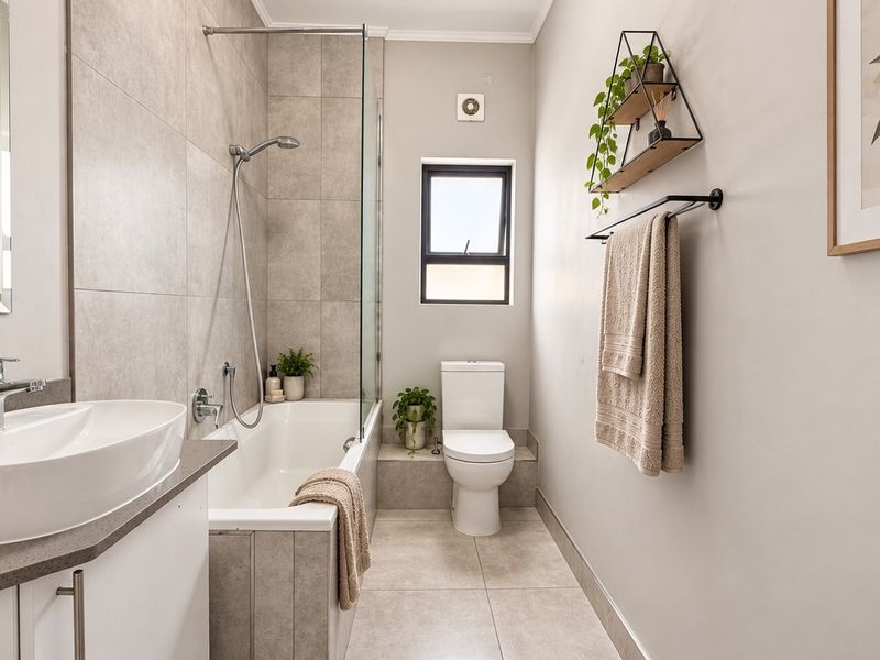 Modern bathroom featuring a built-in vanity, basin, bathtub with shower screen, and toilet, finished with neutral floor and wall tiling.