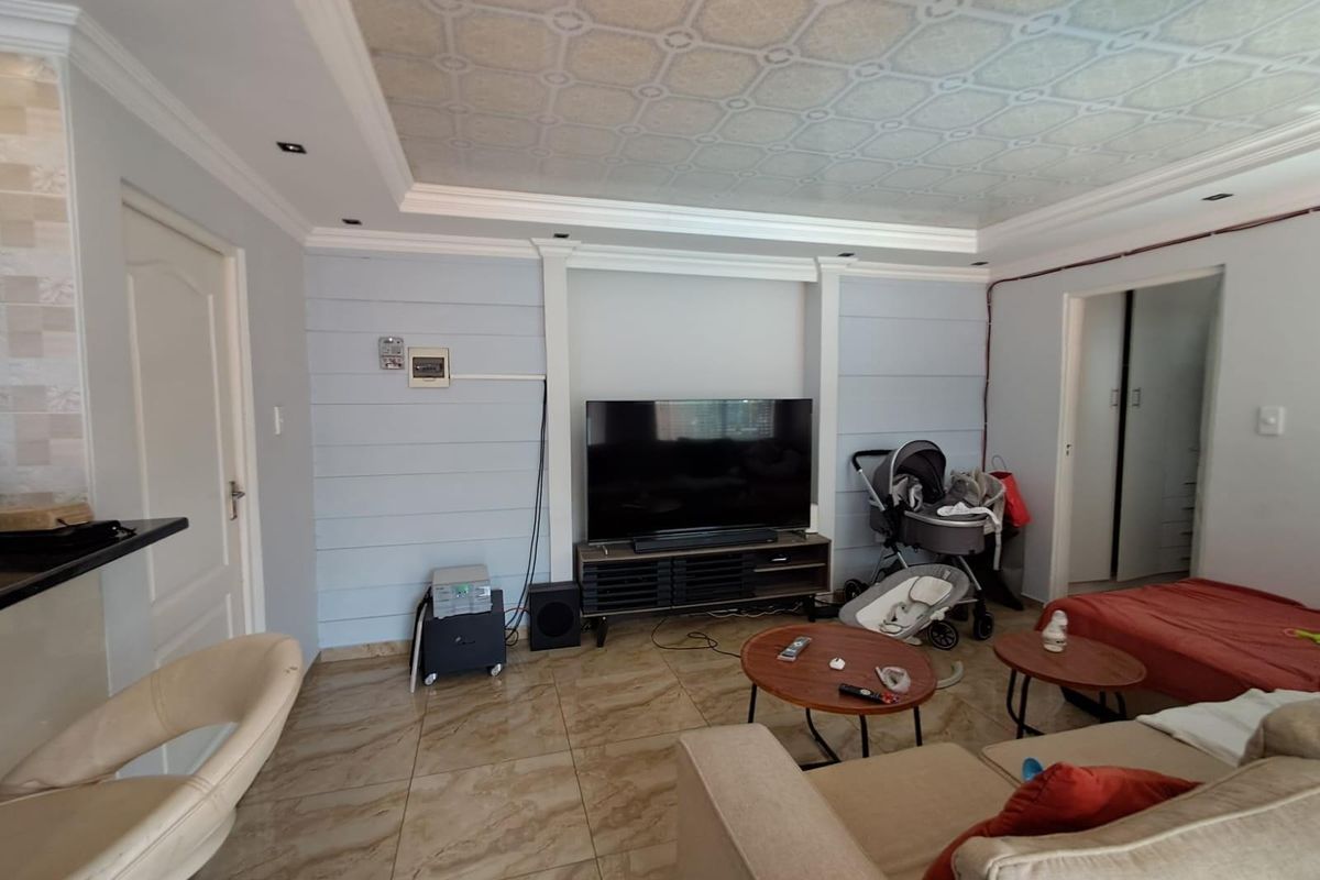 A living room featuring tiled flooring, decorative ceiling paneling, and recessed lighting, providing a functional space for relaxation.